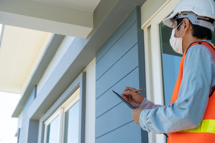 Man in hi-vis vest holding clipboard conducting home inspection checklist