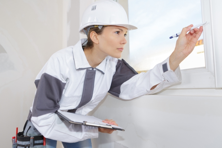 Female home inspector looking at window with pen in hand
